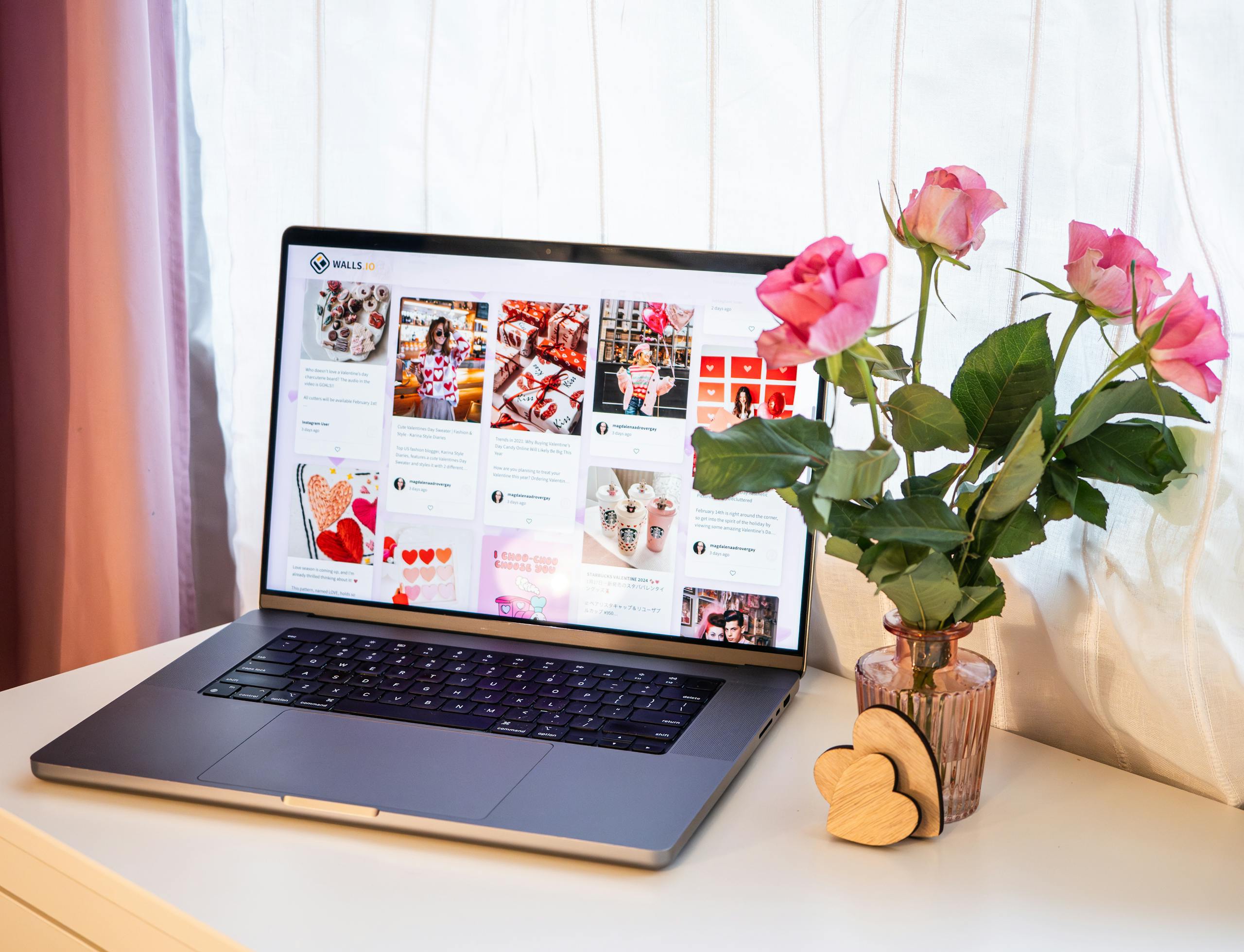 A romantic desk setup featuring pink roses in a vase next to a laptop displaying social media for Valentine's Day.