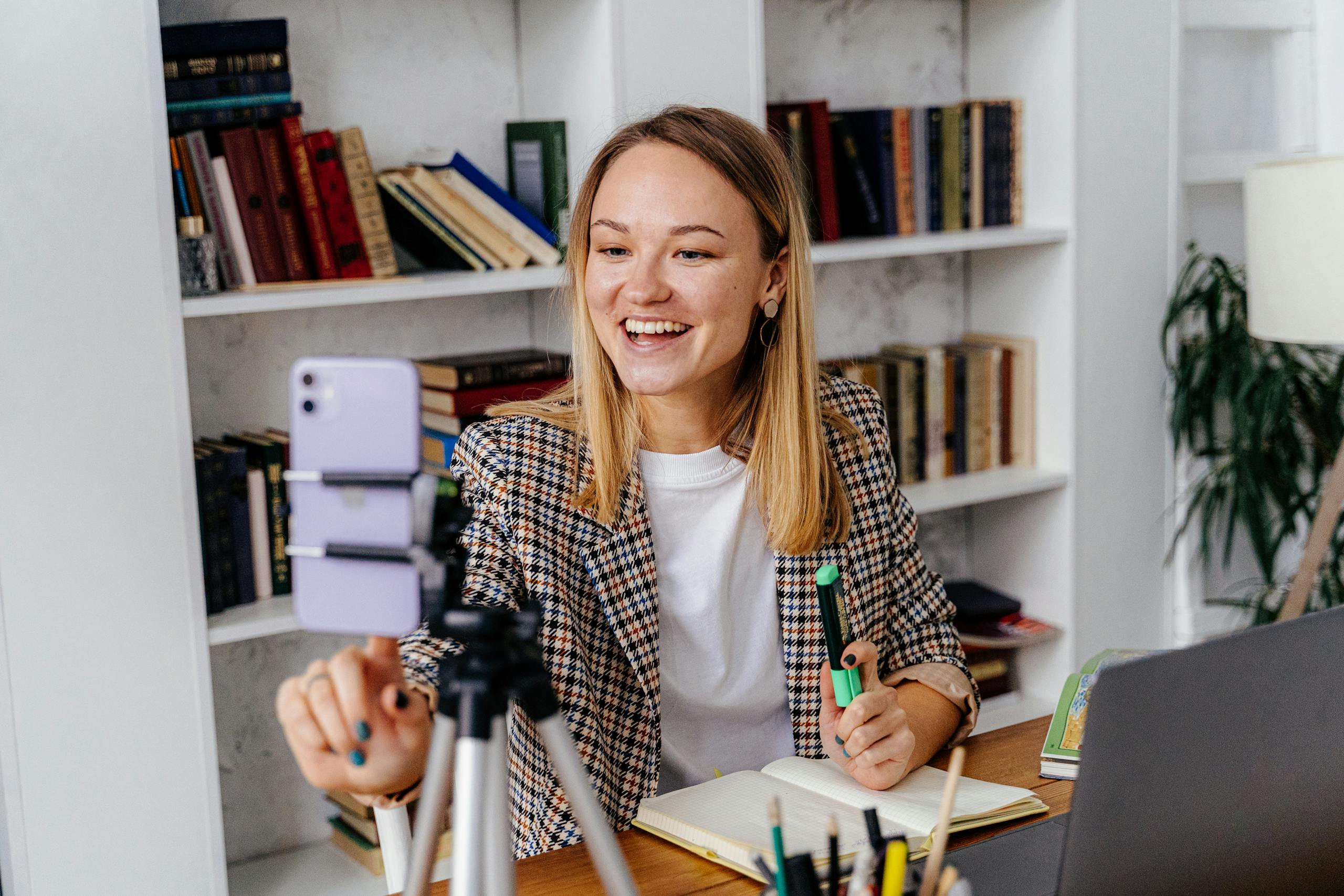 A woman conducts an online lesson from her home office, using a smartphone and a laptop.